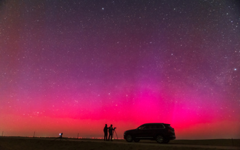 Purple northern lights at night with a shadow of two people and a car. 