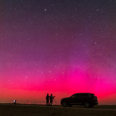 Purple northern lights at night with a shadow of two people and a car. 