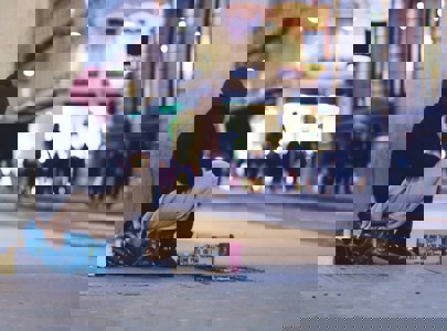 A homeless person sitting on a street corner as people walk by