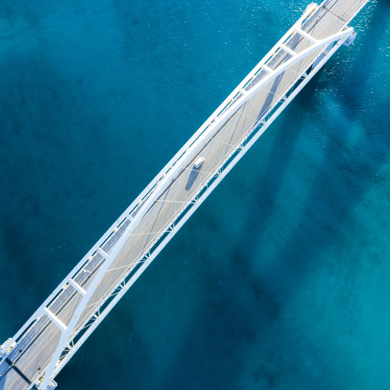 Aerial shot of a white bridge over blue water with a single van crossing the bridge