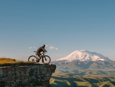 Cyclist At The Ledge Of A Mountain Looking At The Skyline